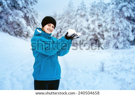 Girl playing with snow in park. A Girl Wearing Warm Winter Clothes holds Snow In Winter Forest. Attractive young woman in wintertime outdoor.