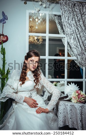 Gorgeous bride blonde in wedding dress in luxury interior with diamond jewelry posing at home and waiting for groom. Romantic brunette bride in a luxurious wedding dress in elegant expensive interior