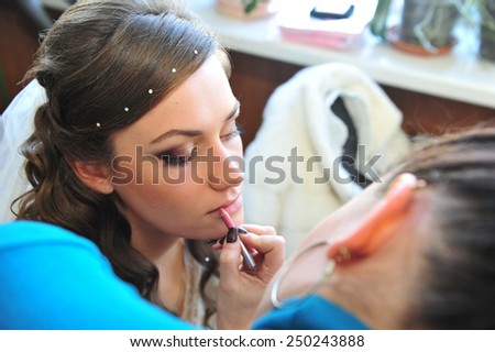Woman applying make up for a bride in her wedding day near mirror. Closeup of a makeup artist applying makeup