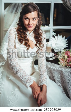 Gorgeous bride blonde in wedding dress in luxury interior with diamond jewelry posing at home and waiting for groom. Romantic rich brunette bride in a luxurious wedding dress in expensive interior