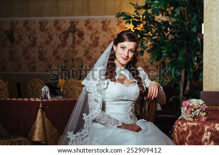 Gorgeous bride blonde in wedding dress in luxury interior with diamond jewelry posing at home and waiting for groom. Rich brunette bride in a luxurious wedding dress in elegant expensive interior