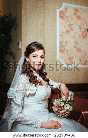 Gorgeous bride blonde in wedding dress in luxury interior with diamond jewelry posing at home and waiting for groom. Rich brunette bride in a luxurious wedding dress in elegant expensive interior