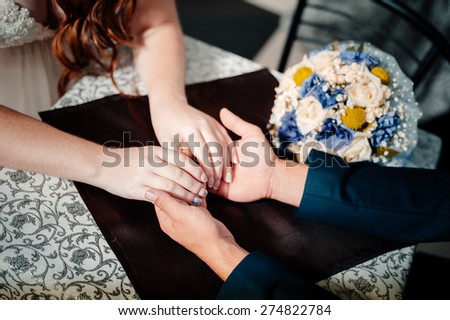 Closeup portrait of groom holding brides hand on table near bouquet.