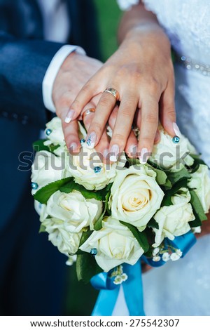 hands of the bride and groom with rings on a beautiful wedding bouquet.