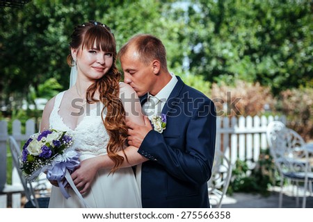 wedding couple kissing in green summer park. bride and groom kissing, standing together outdoors, hugging among green trees. Bride holding wedding bouquet of flowers.