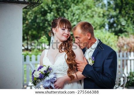 wedding couple kissing in green summer park. bride and groom kissing, standing together outdoors, hugging among green trees. Bride holding wedding bouquet of flowers.