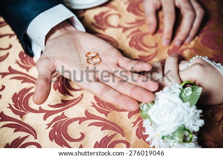 Couple\'s hands on the table and wedding rings and bridal bouquet flowers