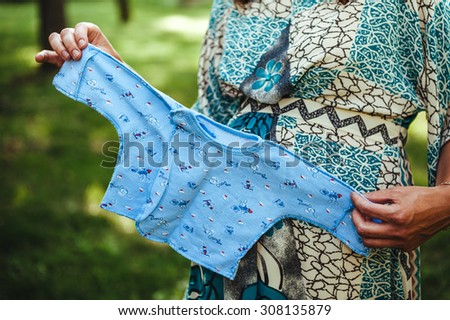 It is a boy! Cropped image of pregnant woman holding little blue shirt near her abdomen. Pregnant woman tummy