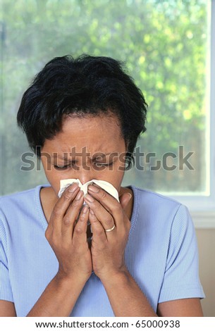 African American woman with cold or allergies sneezing into tissue
