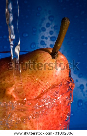 The pear under a water stream, is photographed on a dark blue background