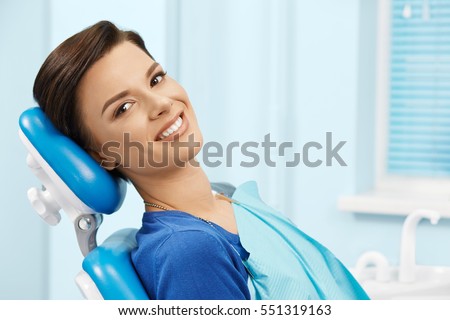 Young female patient visiting dentist office.Beautiful smiling woman with healthy straight white teeth sitting at dental chair.Dental clinic.Stomatology