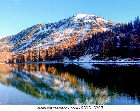 Red larches and snowy peaks are reflected in the alpine lake Montgenevre France
