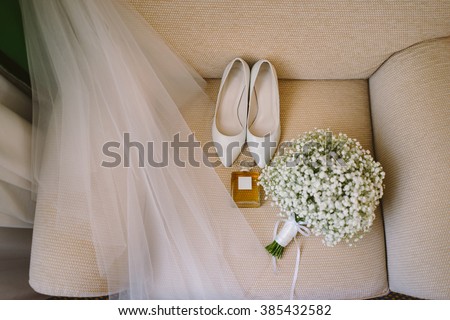 wedding set of bridal bouquet, white shoes, perfume and veil on the beige armchair