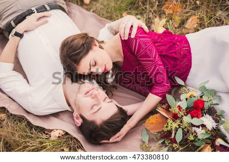 Stylish and romantic caucasian couple lie on the grass and leaves in the beautiful autumn park. Love, relationships, romance, happiness concept.