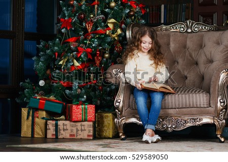 Little girl sitting in a chair and reading a book. New Year\'s Eve. Christmas.