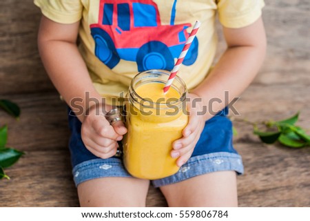 Boy drinking juicy smoothie from mango in glass mason jar with striped red straw on old wooden background. Healthy life concept, copy space.