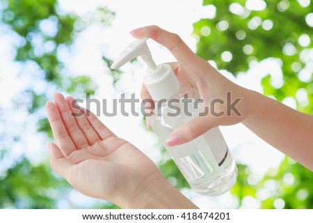 Female using hand press bottle and pouring alcohol-based sanitizer on other hands. Apply all over your hands. Green bokeh background.