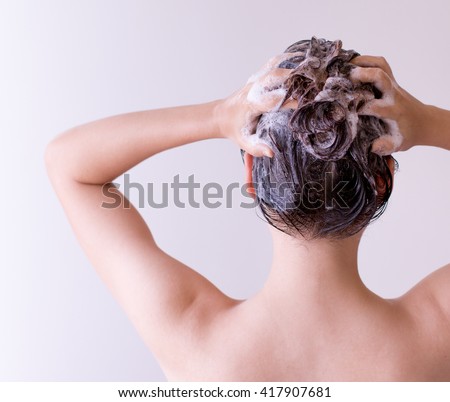 Woman shampooing her hair with both hands on her head in front of a white background.