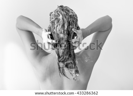 The back of a sexy fit woman washing her hair full of suds in front of a white background