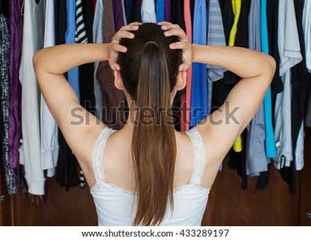 A frustrated young woman standing in front of her closet, trying to decide on her best outfit for a night out with her friends.