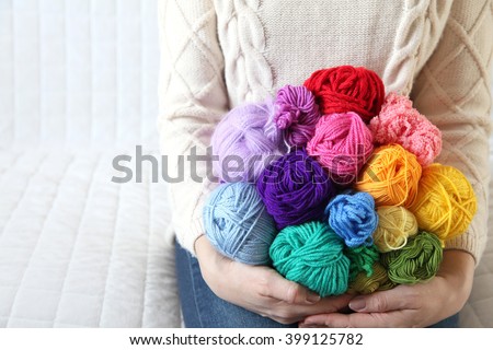 Woman sitting on the couch and holding a colored yarn. Knitted sweater. White background. Knitter.