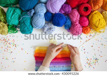Balls of colored yarn. View from above. All the colors of the rainbow. Sample knit. Women\'s hands are knitted. Crochet.