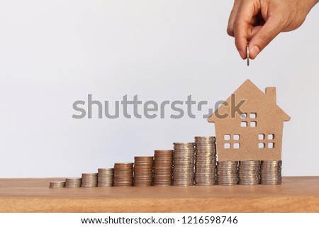 Hand putting money coins to row of coins and house model on wooden table. Concept for property ladder, mortgage and real estate investment