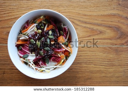 Red salad with carrots, sprouts, pumpkin seeds and seaweed in white bowl on wooden background, free space for text
