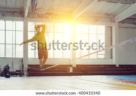Sport, leisure, recreation and healthy active lifestyle concept - man slacklining walking and balancing on a rope, slackline in a sports hall