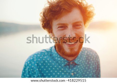 Outdoor portrait of young handsome smiling ginger man with beard