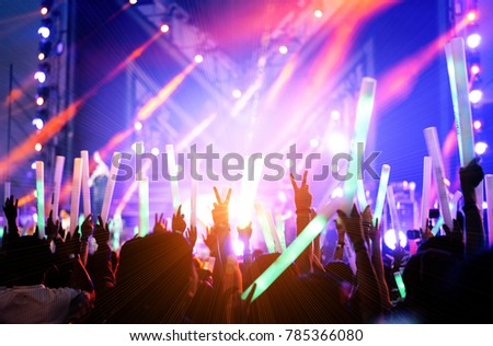 Crowd of hands up concert stage lights and people fan audience silhouette raising hands or glow stick holding in the music festival rear view with spotlight glowing effect