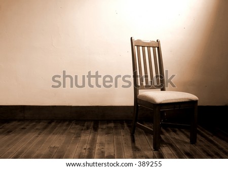 Wooden chair alone in a room lit by only a window.
