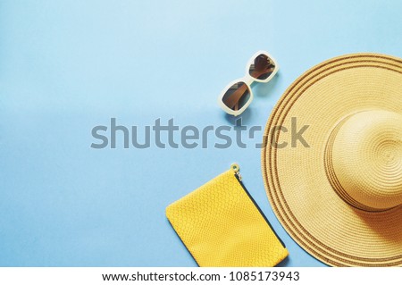 Sun hat, yellow clutch, brown sunglasses on a blue background. Flat lay beach photo. Summer travel concept, free space for text