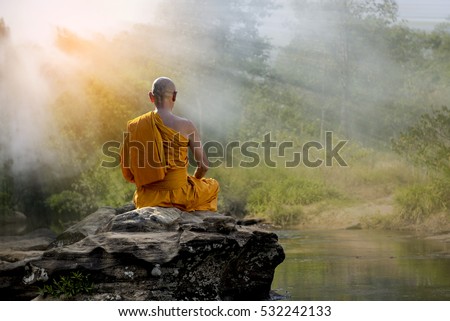 Buddhist monk in meditation at water fall in nature amidst the hot sun .