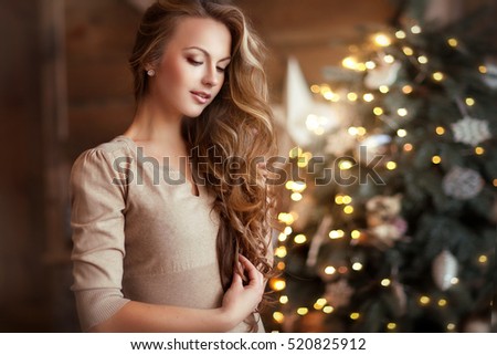 Beautiful young girl  with long curly hair standing on a christmas background with boke lights and looking down. Magic warm new year photo.