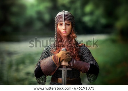 Beautiful red haired girl in metal medieval armor dress with sword standing in warlike pose and looking at camera with fearless. Fairy tale story about warrior . Warm art work.