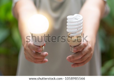 Power saving concept. Hands holding  new  Light Emitting Diode ( LED ) light bulb with light on and blur spiral compact-fluorescent (CFL) bulbs behind for copyspace.
