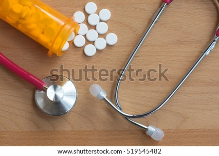 Conventional white round oral medicine, paracetamol, spill from yellow bottle on a wooden background with doctor stethoscope. Medical healthcare concept