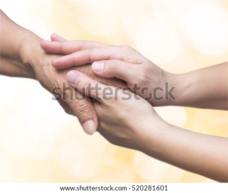 Young female hand holding old hand to comfort her with lens flair effect and golden lights bokeh background.