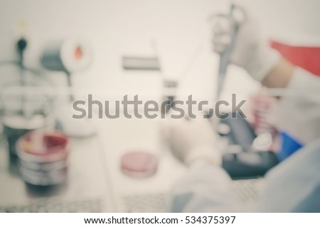 Blur abstract background of scientist or lab worker hand in glove using pipette dropper dropping sample to plate of research laboratory drug resistant testing in bio-safety cabinet in hospital.