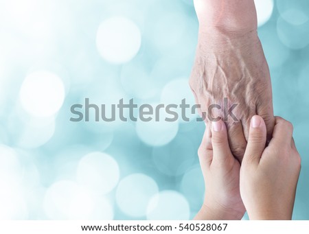 Young child female hands holding old hand to comfort her with lens flair effect and green lights bokeh background.International Day of People with Disability, with copyspace and clipping path