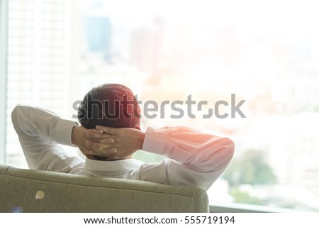Relax business man lifestyle at home sitting on modern chair in living room looking out of window toward beautiful cityscape downtown urban landscape city life w/ sunlight effect: Easy happy people