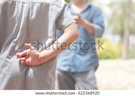 Lie kids concept.Liar female child hand crossing fingers behind back with father in front. lie and cheating, problem child. April Fools\' Day