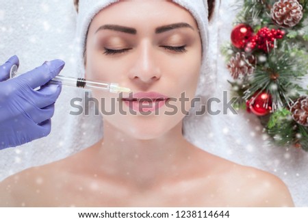 The cosmetologist makes injections in the lips of the patient.  Closeup woman face and new year wreath.