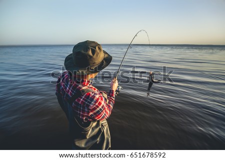 A fisherman with a fishing rod in his hand and a fish caught stands in the water