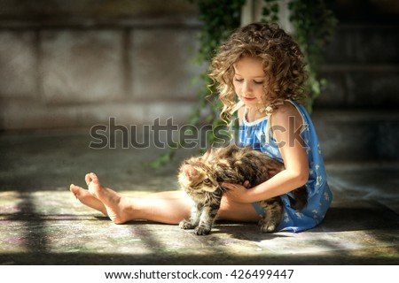 girl with curly hair in a blue sundress played with little fluffy cat in the yard. Retro