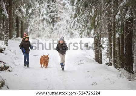 two brothers dressed in fur coats and jackets running with his dog on the winter snow-covered forest