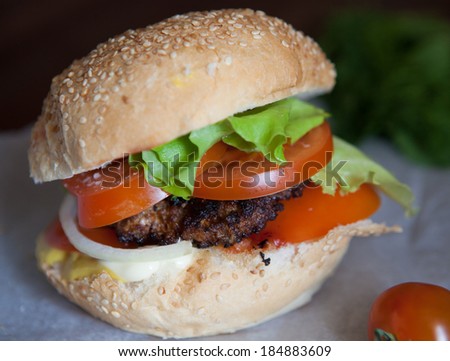 Burger with lettuce, onions, tomato and pickles on a sesame seed bun.