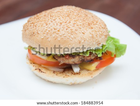 Burger with lettuce, onions, tomato and pickles on a sesame seed bun.