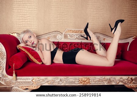 Blonde beautiful woman on red sofa wearing black bra. Cabaret style